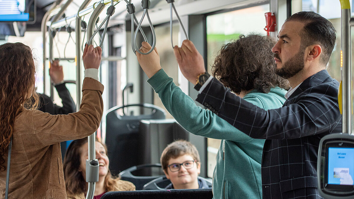 Tre passeggeri in piedi in autobus si sorreggono ai sostegni.