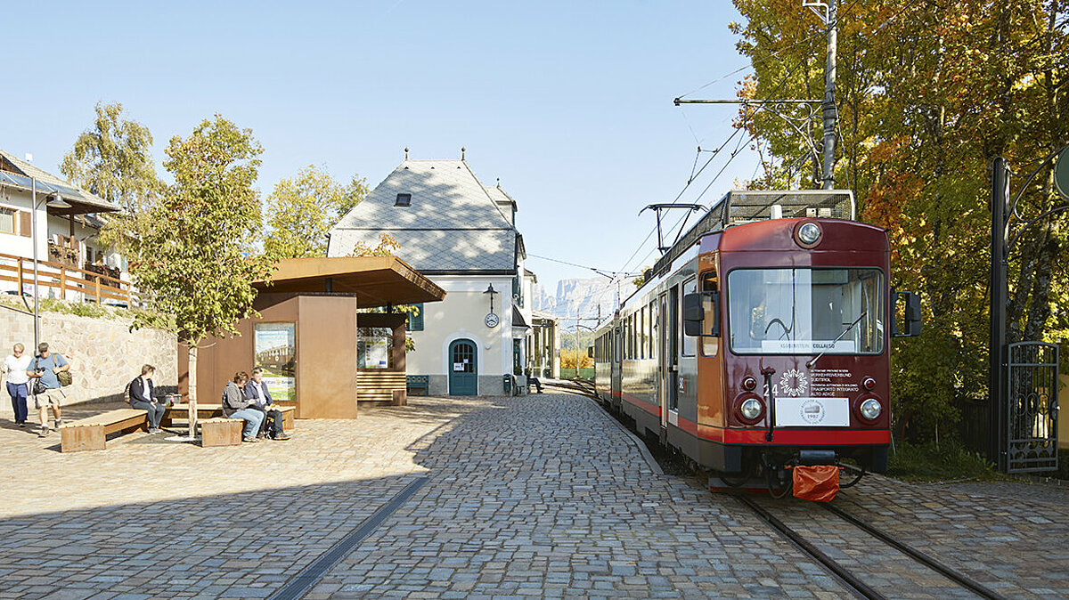 Persone in attesa alla fermata di Soprabolzano. Trenino del Renon in partenza.