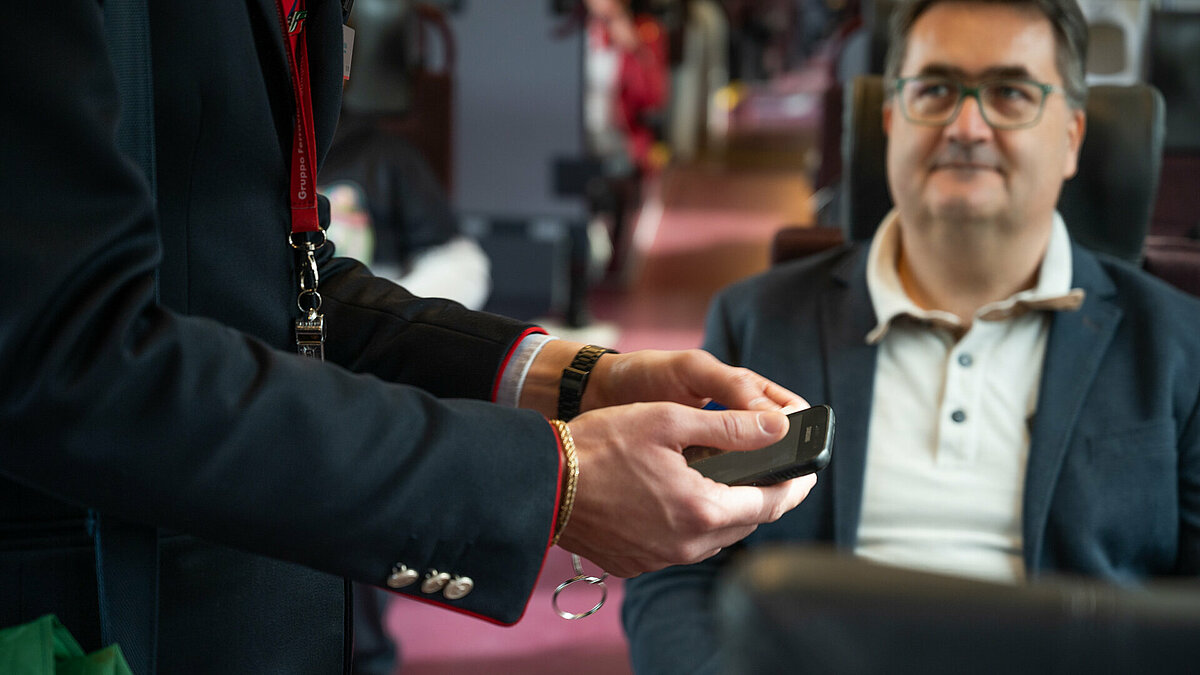 Un controllore controlla un biglietto sullo smartphone, mentre un passeggero attende.