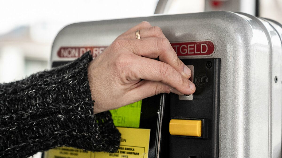 Una persona acquista un biglietto alla biglietteria automatica su un autobus. Si vede la mano che inserisce delle monete nella fessura.