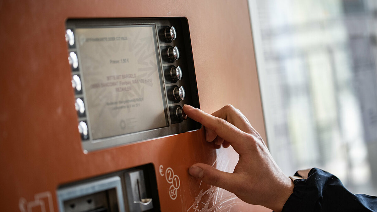 Particolare della mano di una persona intenta a scegliere un'opzione a lato dello schermo di una biglietteria automatica.