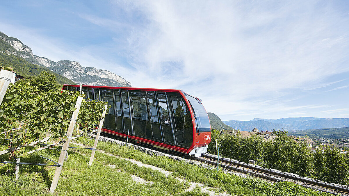 Cabina della funicolare della Mendola, vista dal lato, leggermente coperta dalla vegetazione.