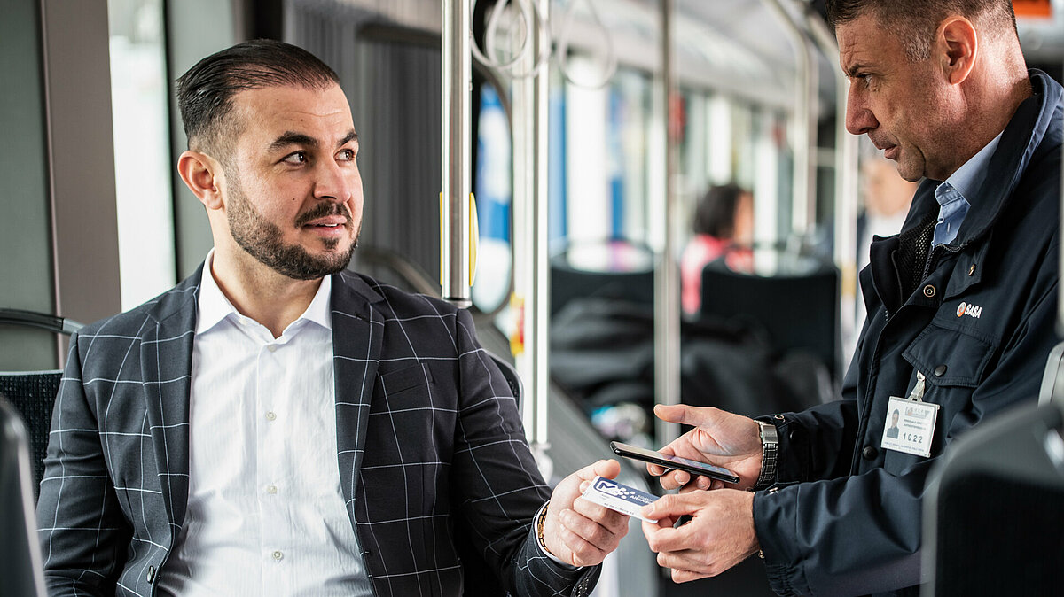 Un controllore in autobus controlla il biglietto di un passeggero seduto.